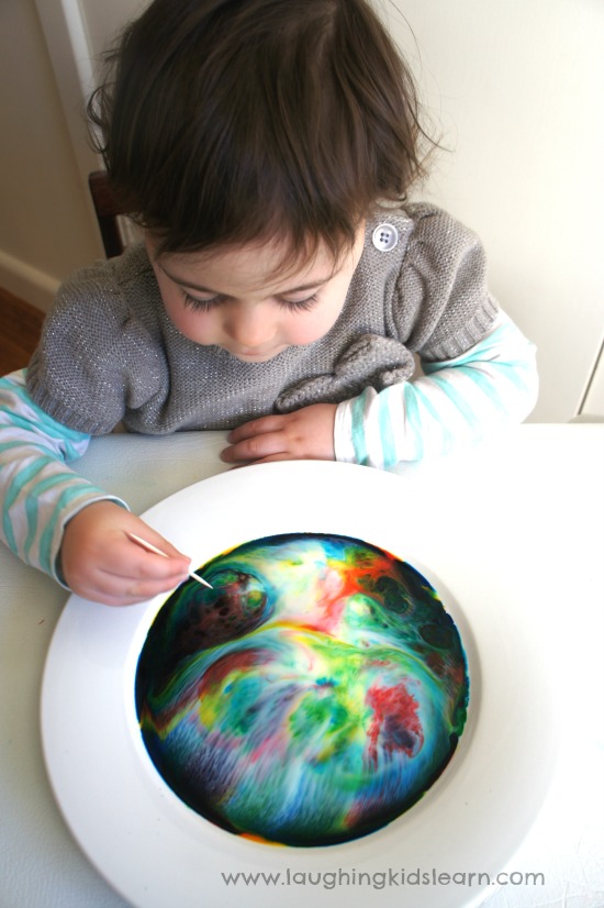 Colour changing magic milk science experiment for kids. Using toothpick to swirl it around. 