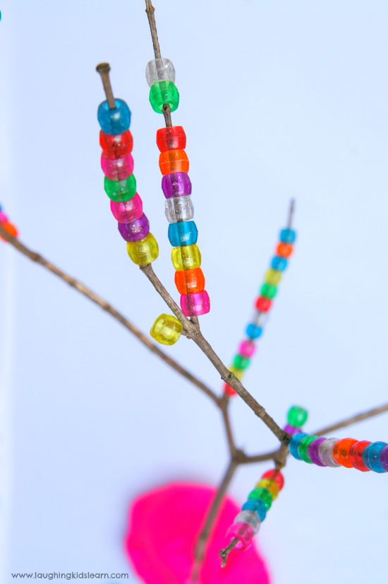 Threading pony beads on a tree branch for fine motor development