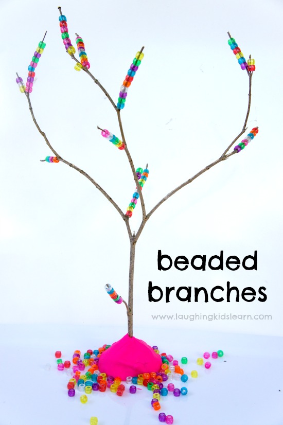 Threading pony beads on tree branches to build fine motor skills