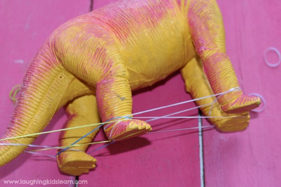 Stretching loom elastic bands around dinosaur figurines. improve small muscles in the hand