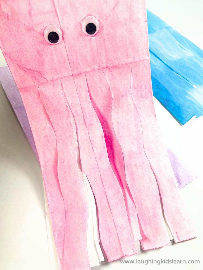 Child's hands crafting a paper bag jellyfish with colorful tissue paper, a popular kids' activity.